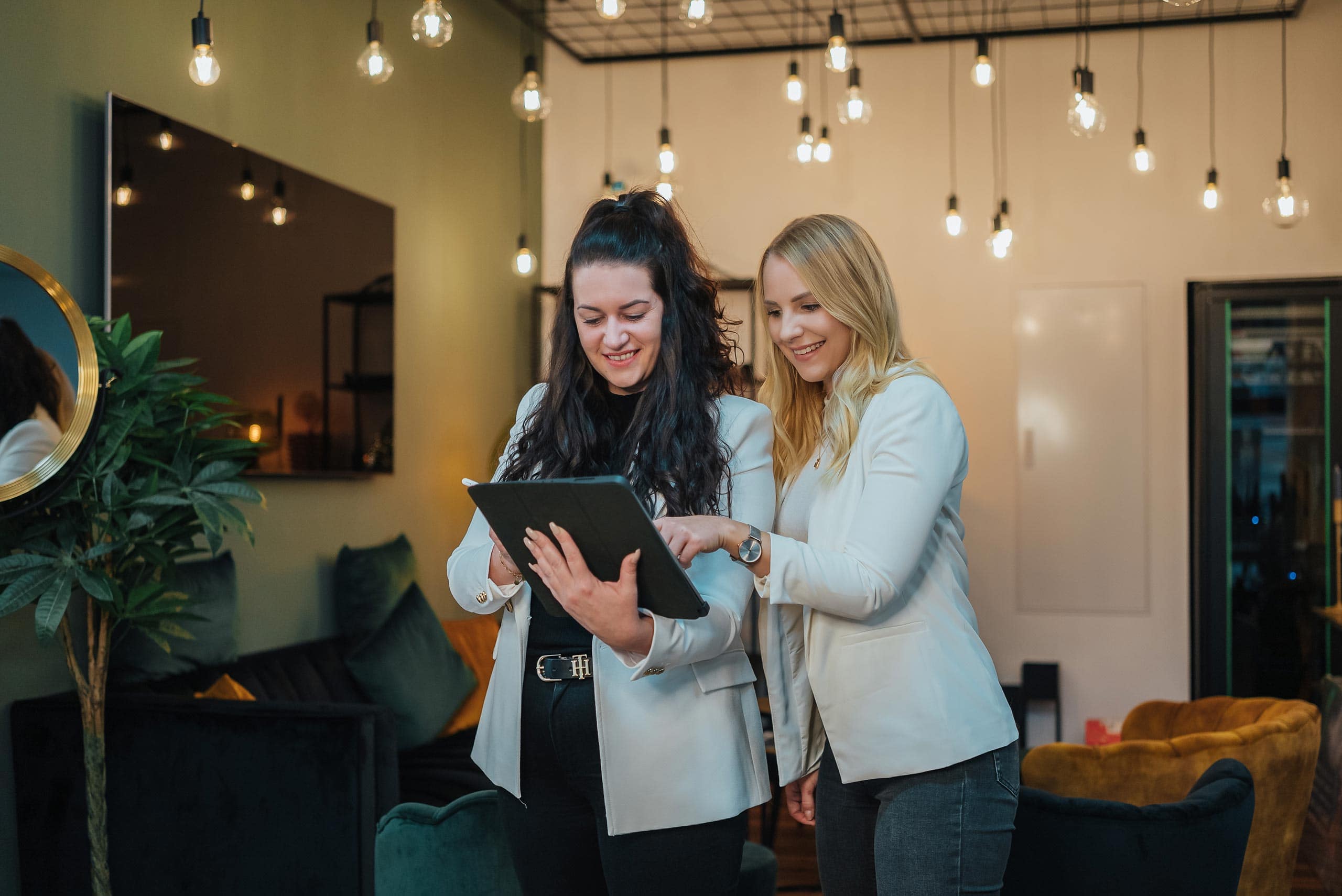 Madeleine und Isabelle stehen in der Agentur-Lounge und auf das iPad Madeleine und Isabelle stehen in der Agentur-Lounge und auf das iPad